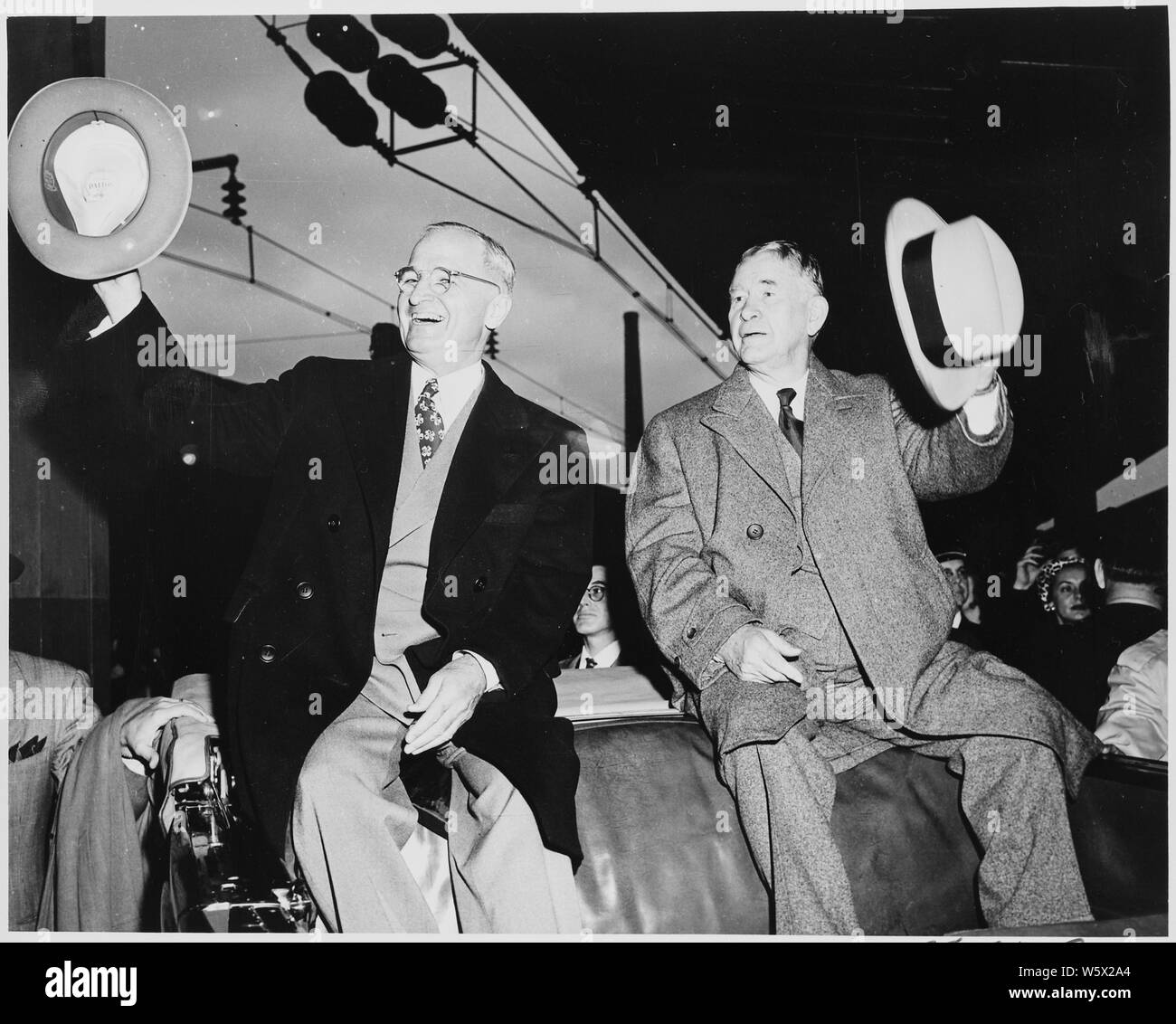 Presdient Harry S. Truman and Vice President-elect Alben W. Barkley in the Washington, DC train station, sitting on the back of an open vehicle, waving their hats to the crowd. Truman and Barkley had just returned to Washington after winning the 1948 election. Stock Photo