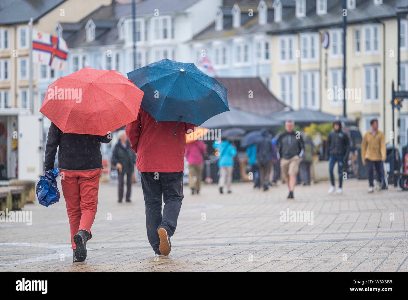 Aberystwyth, Wales, UK. 30th July 2019.  Holidaymakers  in their raincoats and umbrellas walking along the promenade in Aberystwyth in the rain as a belt of thundery and very wet weather spreads across much of the central parts of the UK, bringing with it the risk of disruptive flooding and treacherous driving conditions.. Photo credit : Keith Morris/Alamy Live News Stock Photo