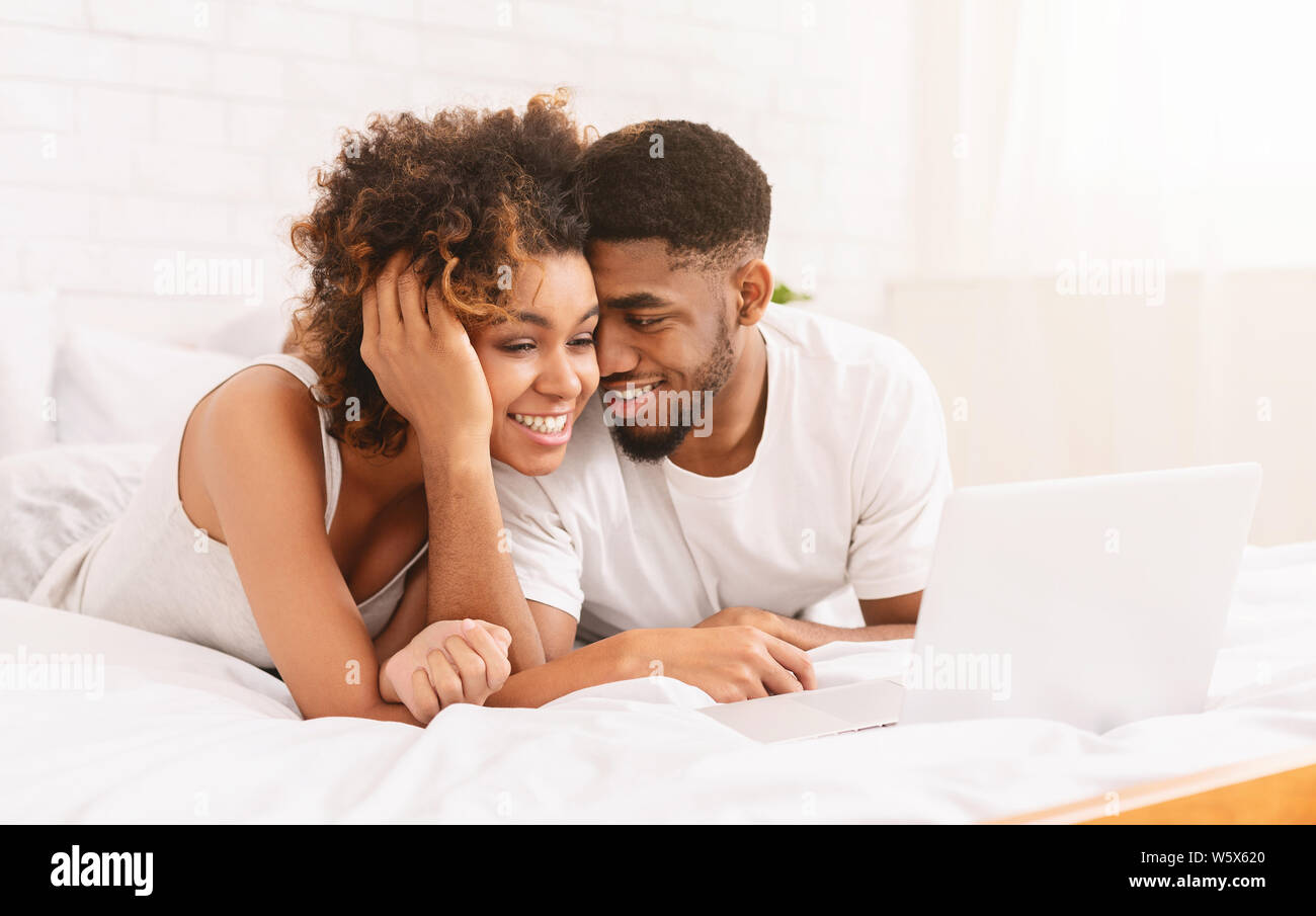 Young black couple lying on bed and using laptop Stock Photo - Alamy