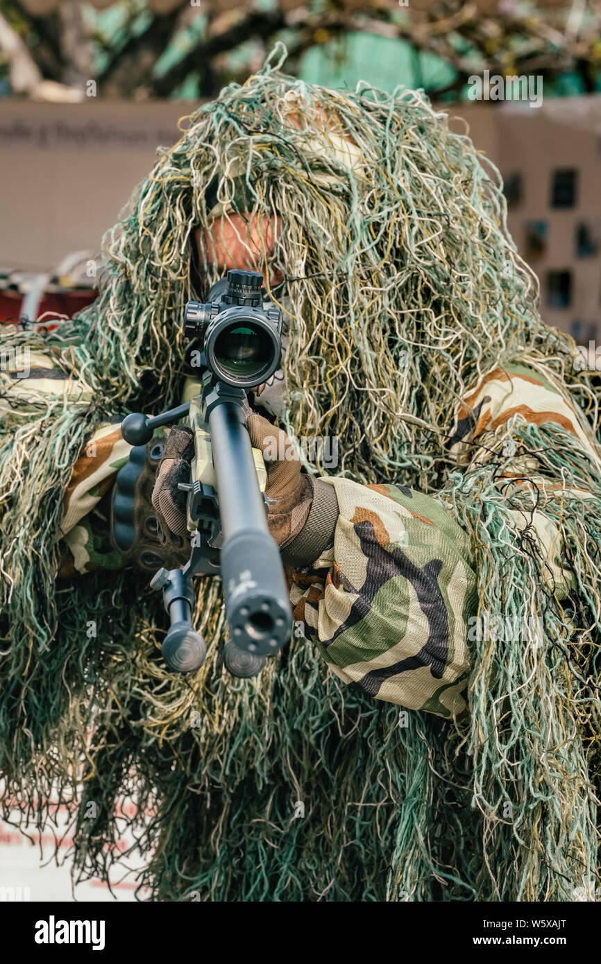 Camouflaged sniper keeps victim at gunpoint. Soldier dressed in ghillie camouflage on nature Stock Photo