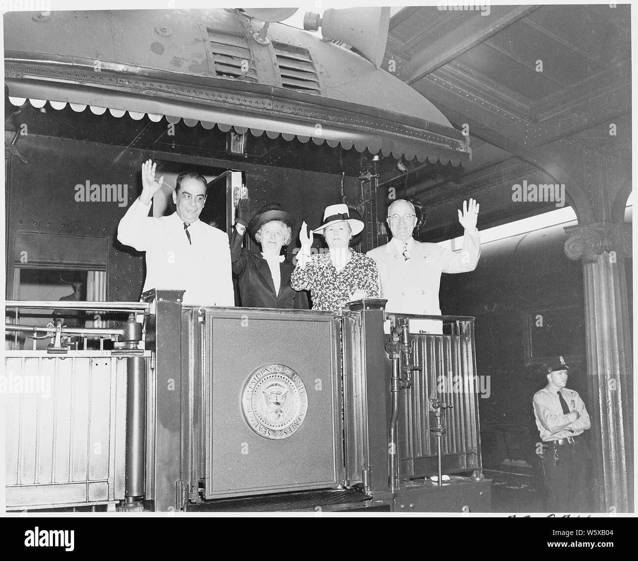 President and Mrs. Harry S. Truman and President and Mrs. Romulo Gallegos of Venezuela, standing on the rear platform of the presidential train, Bolivar, Missouri. President Truman dedicated a statue of Simon Bolivar during his visit to Bolivar, Missouri. A close-up of the two presidents and their wives; everyone is waving. Stock Photo
