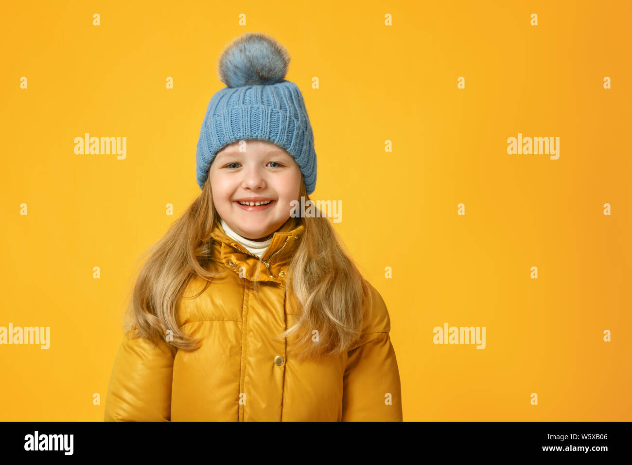 Portrait of a cheerful little girl in jacket and knitted hat over yellow background. Autumn concept. Stock Photo