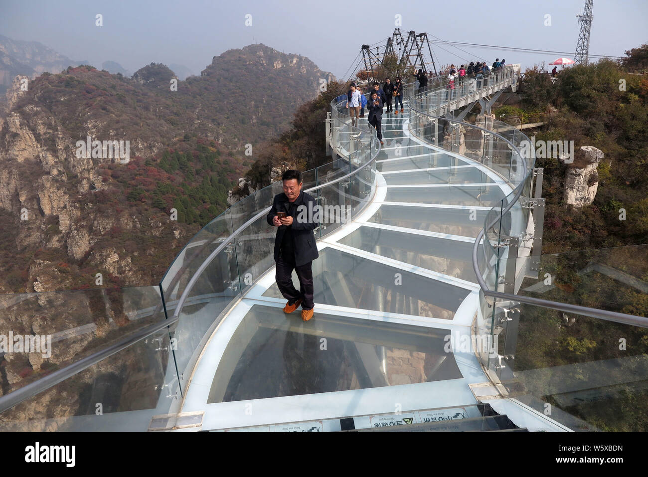 Tourists walk on the glass skywalk 'suspended' in the air along the cliff of Mount Langya in Baoding city, north China's Hebei province, 16 October 20 Stock Photo