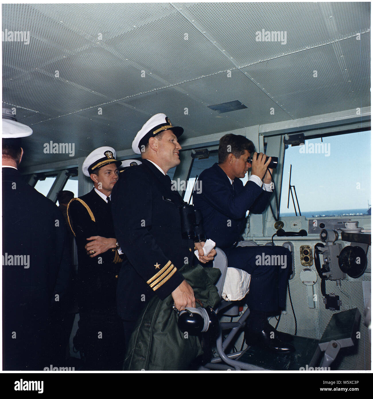 President views Atlantic Fleet Manuevers. Naval Aide Commander Tazewell Shepard, Commander Lang, President Kennedy. Aboard the USS Enterprise. Stock Photo