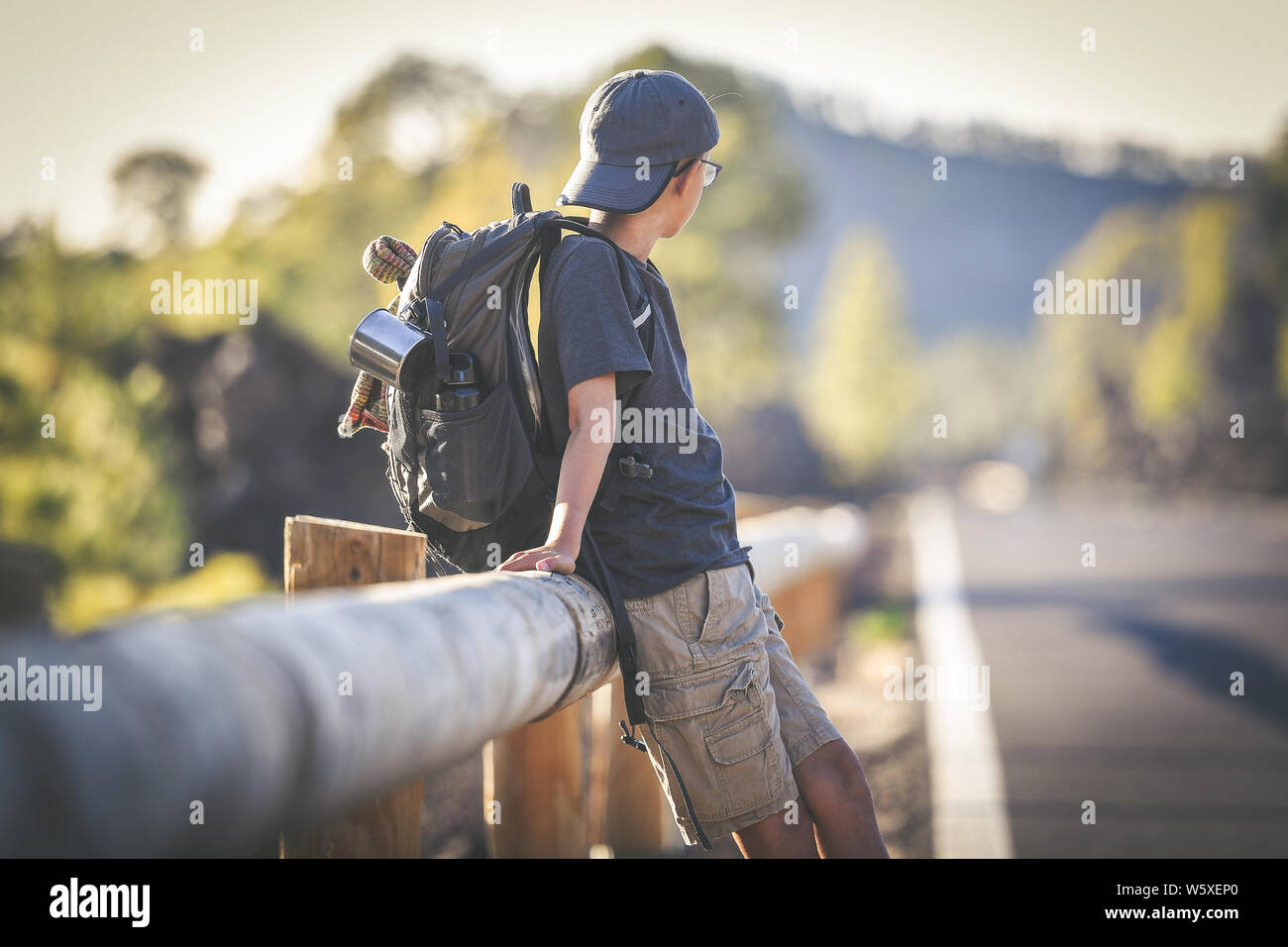 Young boy alone waiting for a ride on the side of the street. Teen with ...