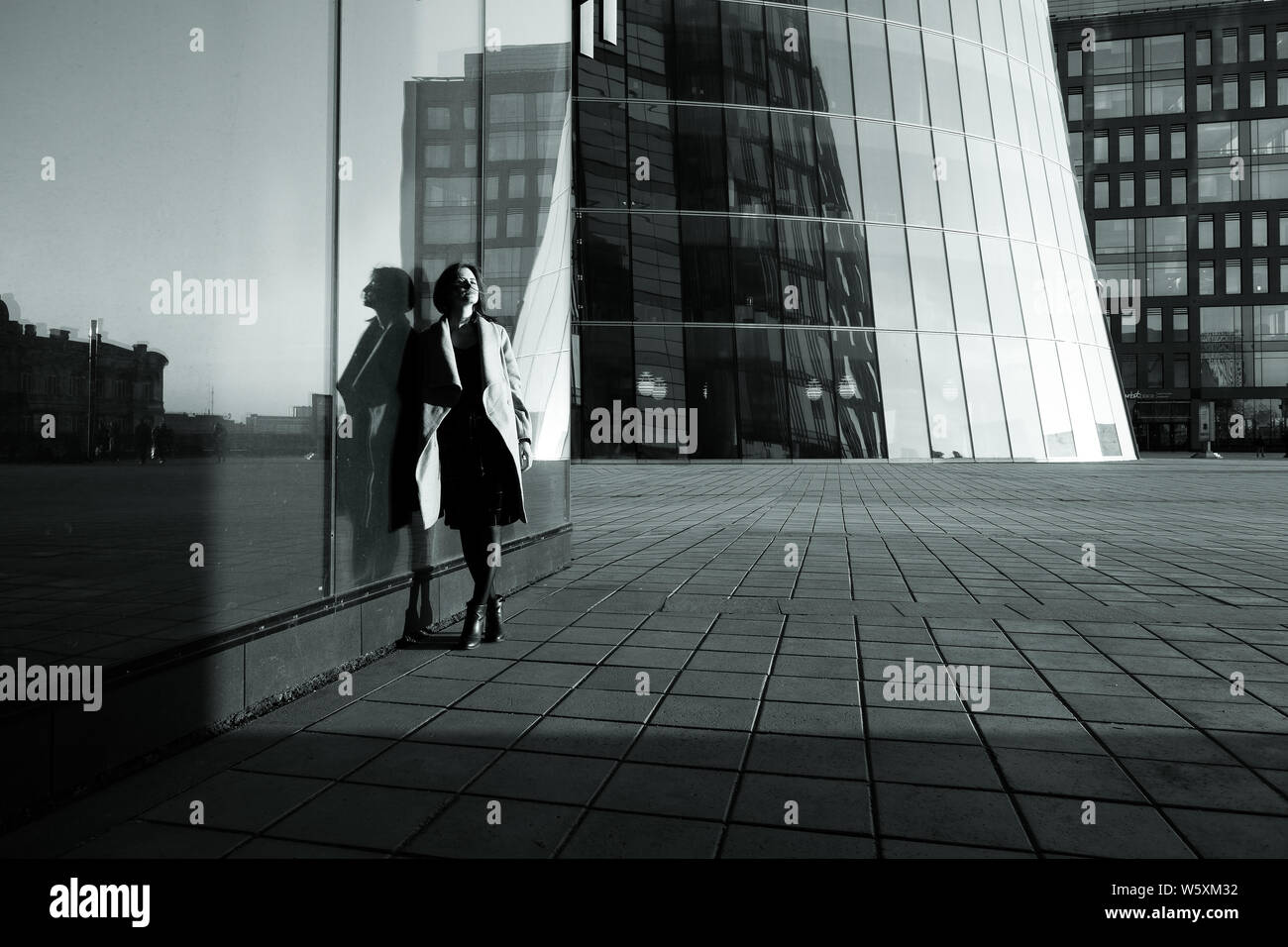Black and white photo of a girl in a coat reflecting in the building against the business center Stock Photo
