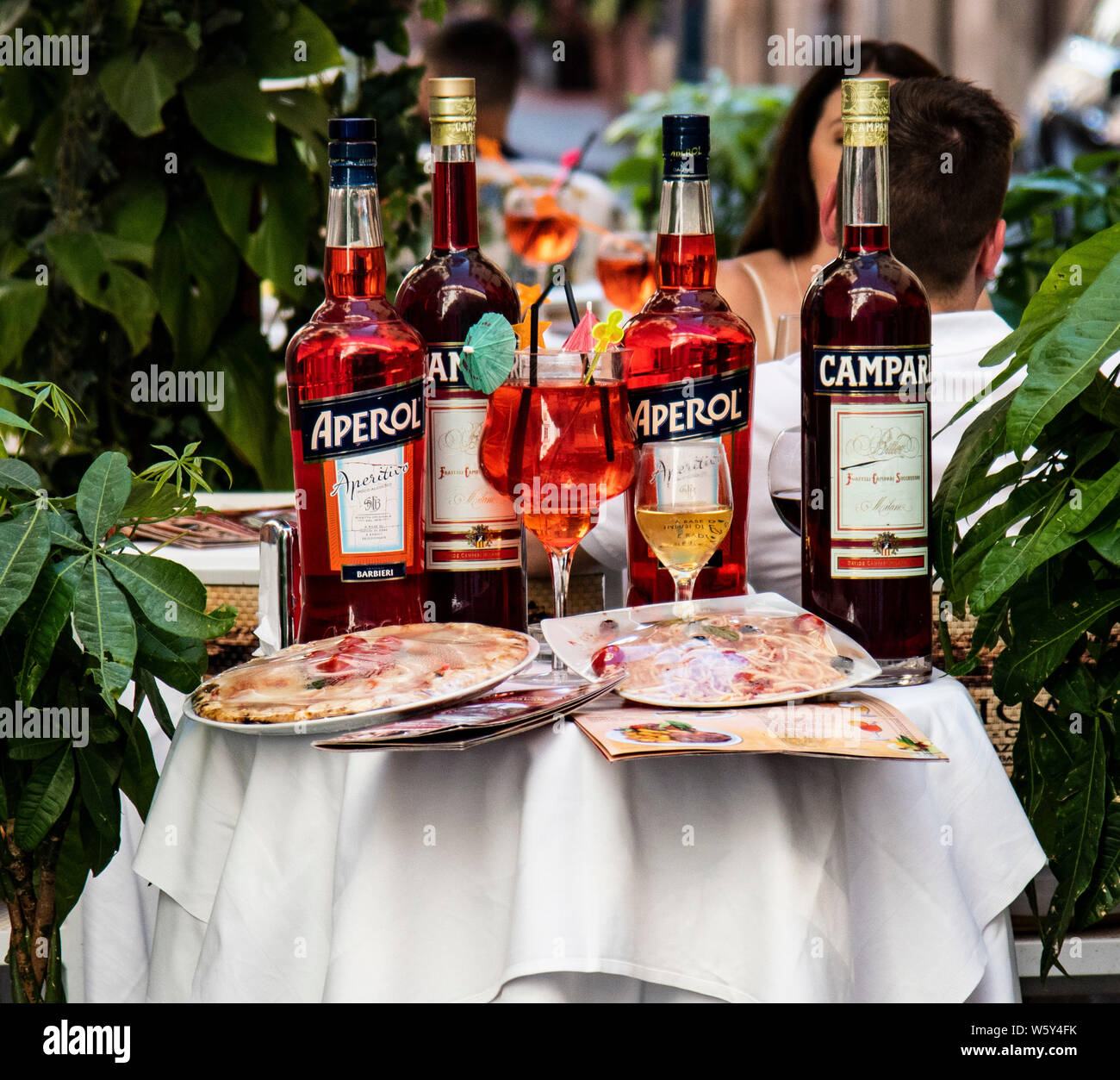 Bottles of Campri and Aperol on a table along pizza's and menus outside a cafe in Rome, italy Stock Photo