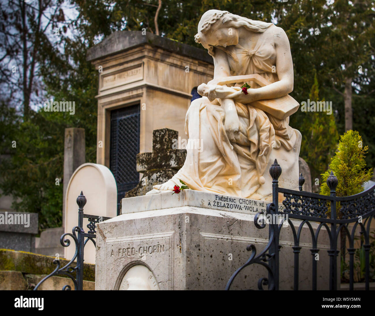 Marble figure of a mourning woman at the grave of composer Frédéric Chopin at the Père-Lachaise Cemetery in Paris, with red roses and a wrought-iron railing in front. Taken on 18 February 2012. Stock Photo