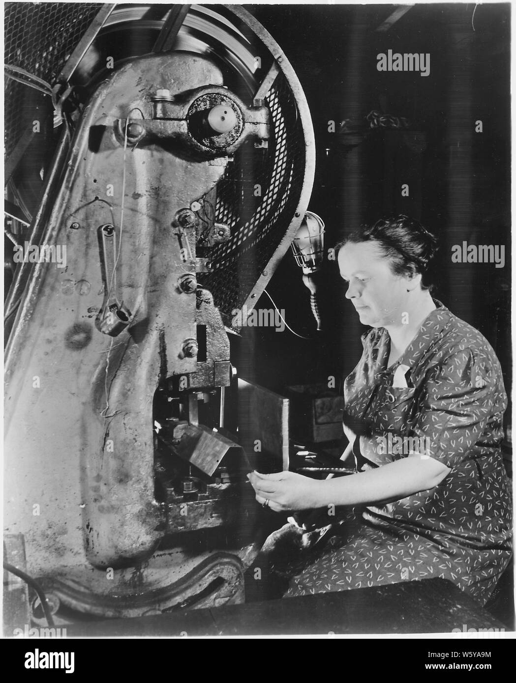 The hand that rocks the cradle can also rock the Axis. American women are rapidly taking their places on the industrial front. Here in this small factory, the owner's wife operates one of the machines making dies for incendiary bombs. Stock Photo