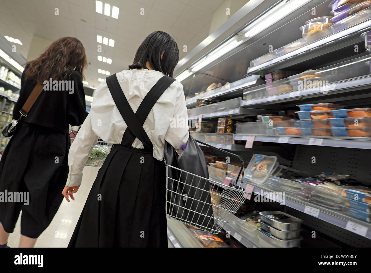 Rear view of two young women customers person shopping in Waitrose supermarket refrigeration aisle London England UK  KATHY DEWITT Stock Photo