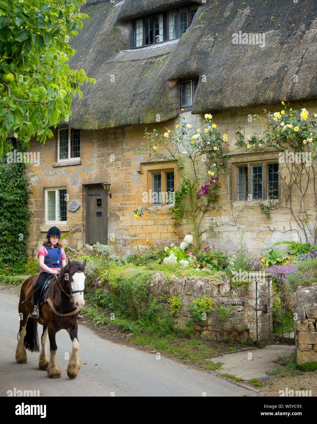 Girl on horseback below thatched roof cottage, Stanton, the Cotswolds, Gloucestershire, England Stock Photo