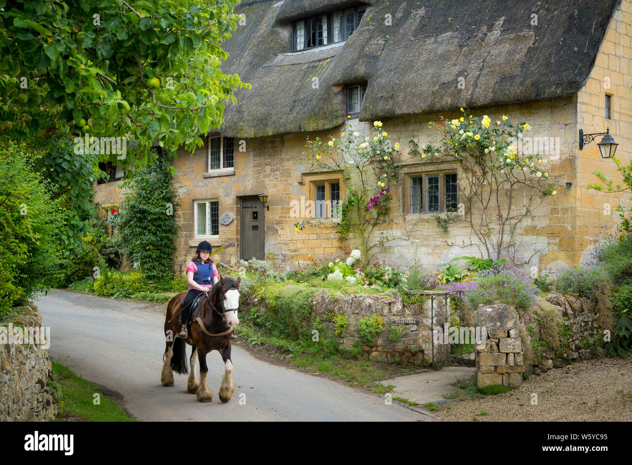 Girl on horseback below thatched roof cottage, Stanton, the Cotswolds, Gloucestershire, England Stock Photo