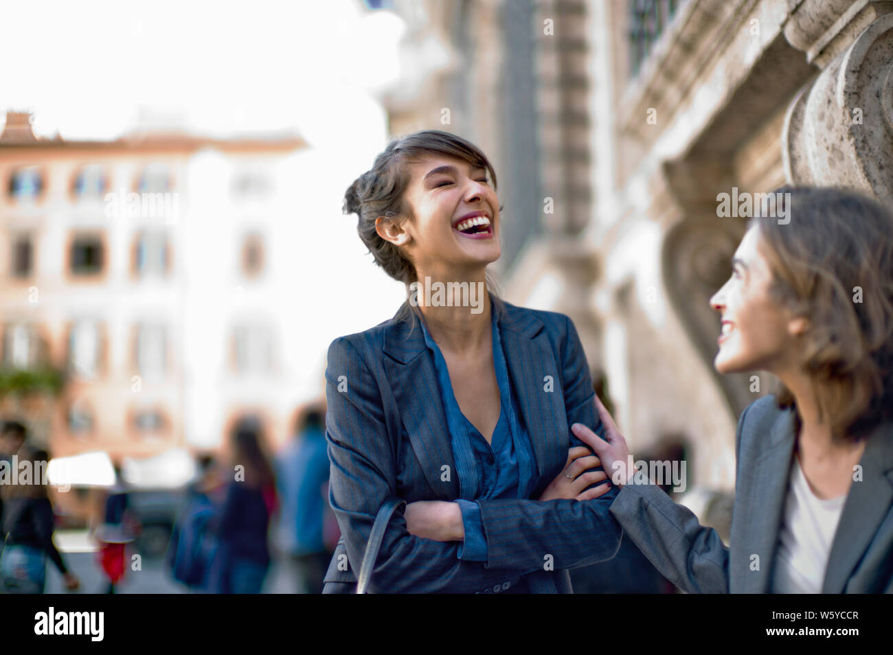 Two young office girls laugh together as they catch up in the city. Stock Photo