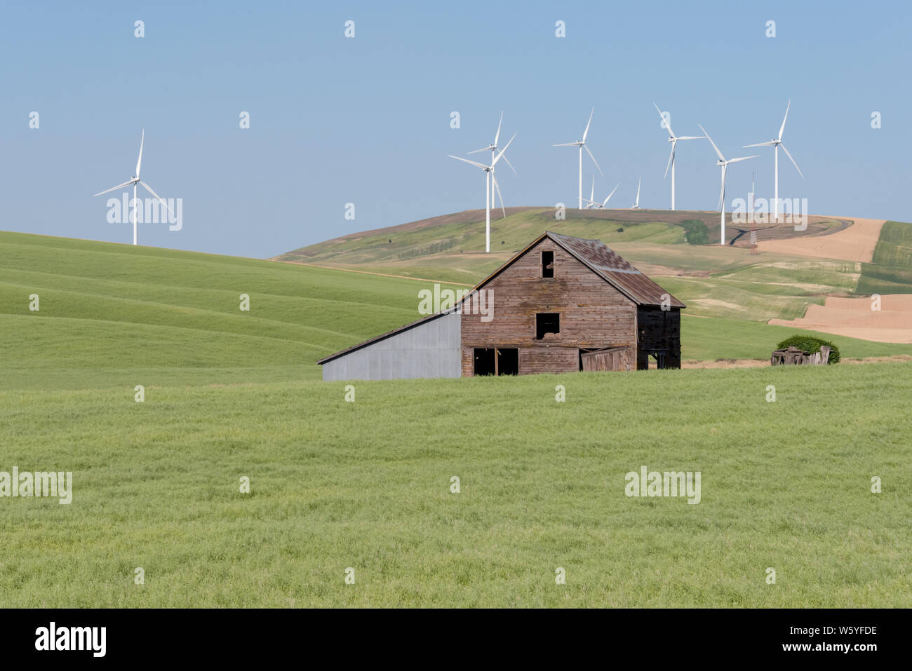 Agricultural Fields and a Barn with a Wind Farm on rolling hills above. Stock Photo