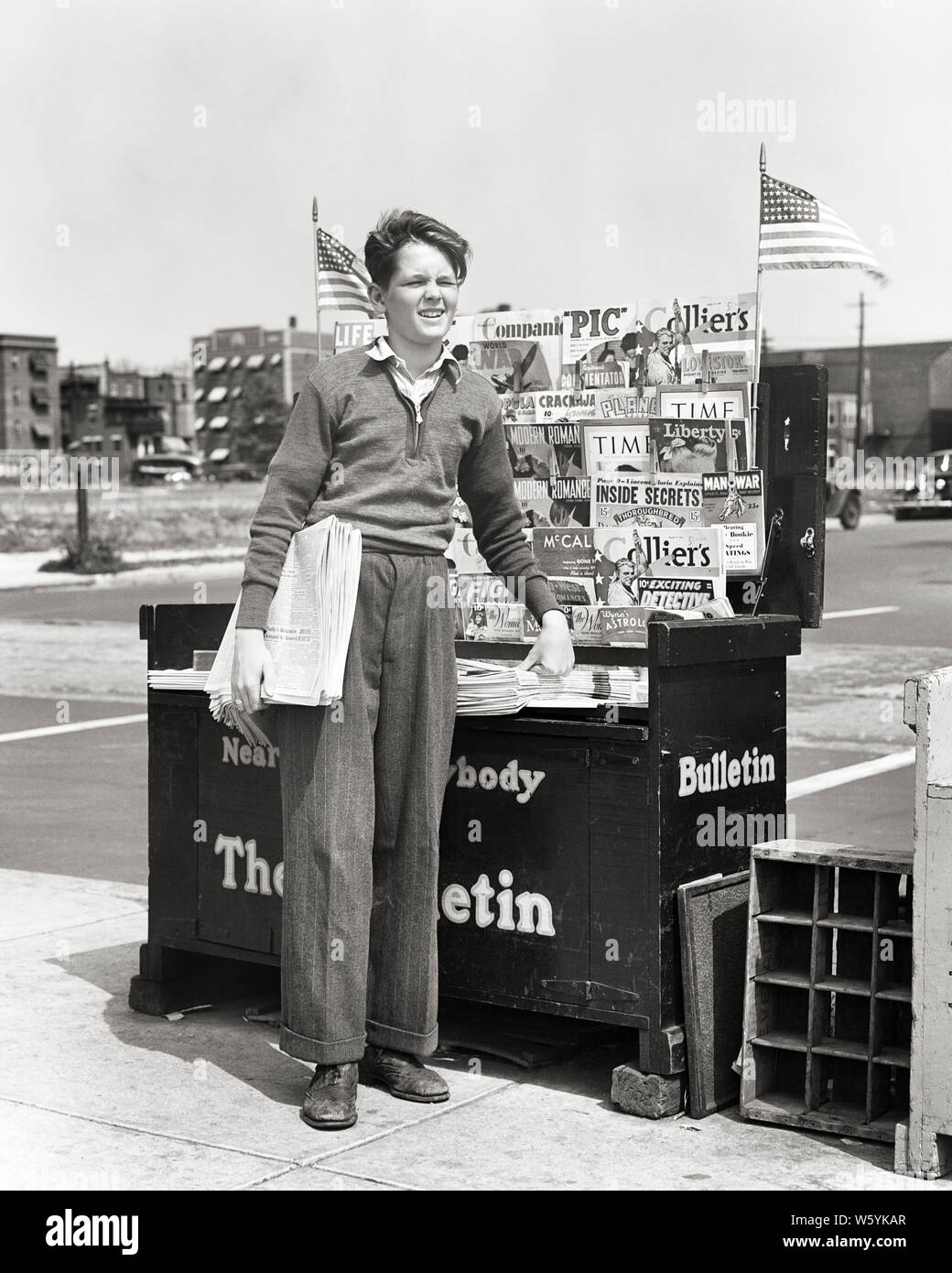 1940s ENTERPRISING BOY STANDING BY NEWSPAPER AND MAGAZINE CORNER NEWSSTAND SELLING DAILY EVENING PAPERS PHILADELPHIA PA USA - b11520 HAR001 HARS FLAGS INFORMATION LIFESTYLE JOBS COPY SPACE FULL-LENGTH PERSONS MALES CORNER B&W GOALS SKILL OCCUPATION SELLING SKILLS AND LEADERSHIP PA NEWSSTAND PRIDE BY OPPORTUNITY OCCUPATIONS CONCEPTUAL HAWKING TEENAGED PART-TIME ENTERPRISING JUVENILES PRE-TEEN RED WHITE AND BLUE STARS AND STRIPS AFTERNOON BLACK AND WHITE CAUCASIAN ETHNICITY DAILY HAR001 OLD FASHIONED Stock Photo