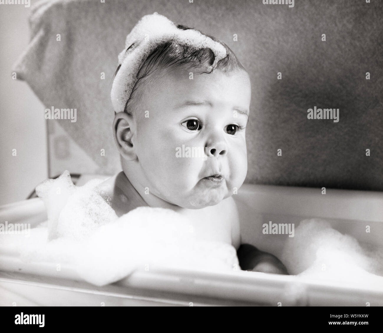 1960s PERPLEXED BABY FUNNY FACIAL EXPRESSION SITTING IN BATHING TUB