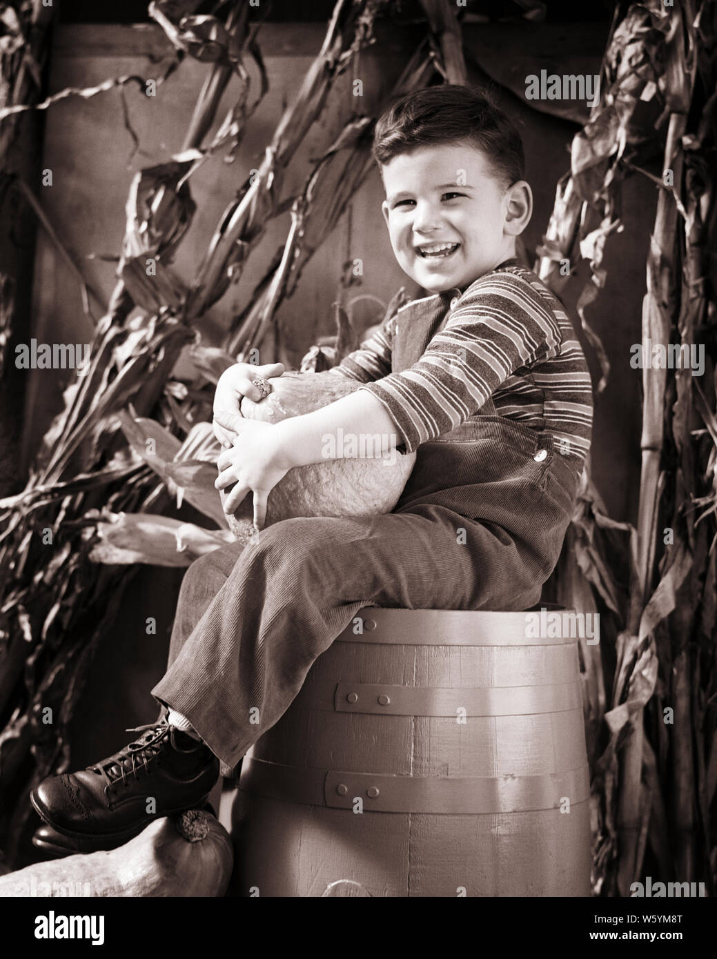 1940s SMILING HAPPY BOY SITTING ON BARREL HOLDING AUTUMN HARVEST PUMPKIN LOOKING AT CAMERA - c1722 HAR001 HARS BARREL EXPRESSIONS AGRICULTURE B&W EYE CONTACT HAPPINESS CHEERFUL EXCITEMENT ON SMILES CONCEPTUAL JOYFUL STYLISH GROWTH JUVENILES BLACK AND WHITE CAUCASIAN ETHNICITY HAR001 OLD FASHIONED Stock Photo