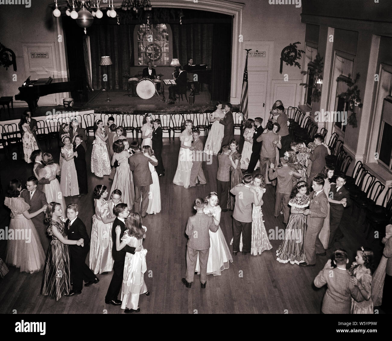 1950s TEENAGE COUPLES GIRLS AND BOYS IN FORMAL DRESSES AND SUITS DANCING AT HIGH SCHOOL SENIOR PROM WITH LIVE BAND IN AUDITORIUM - d2752 LAN001 HARS MAGIC OLD TIME BUSY FUTURE NOSTALGIA BALLROOM OLD FASHION JUVENILE BALANCE SUITS JOY LIFESTYLE CELEBRATION FEMALES HEALTHINESS UNITED STATES COPY SPACE FULL-LENGTH PERSONS UNITED STATES OF AMERICA MALES TEENAGE GIRL TEENAGE BOY ENTERTAINMENT B&W NORTH AMERICA DRESSES NORTH AMERICAN SCHOOLS WIDE ANGLE TEMPTATION SUIT AND TIE DREAMS HAPPINESS HIGH ANGLE AND EXCITEMENT RECREATION AT IN HIGH SCHOOL HIGH SCHOOLS AUDITORIUM CONCEPTUAL AWKWARD STYLISH Stock Photo