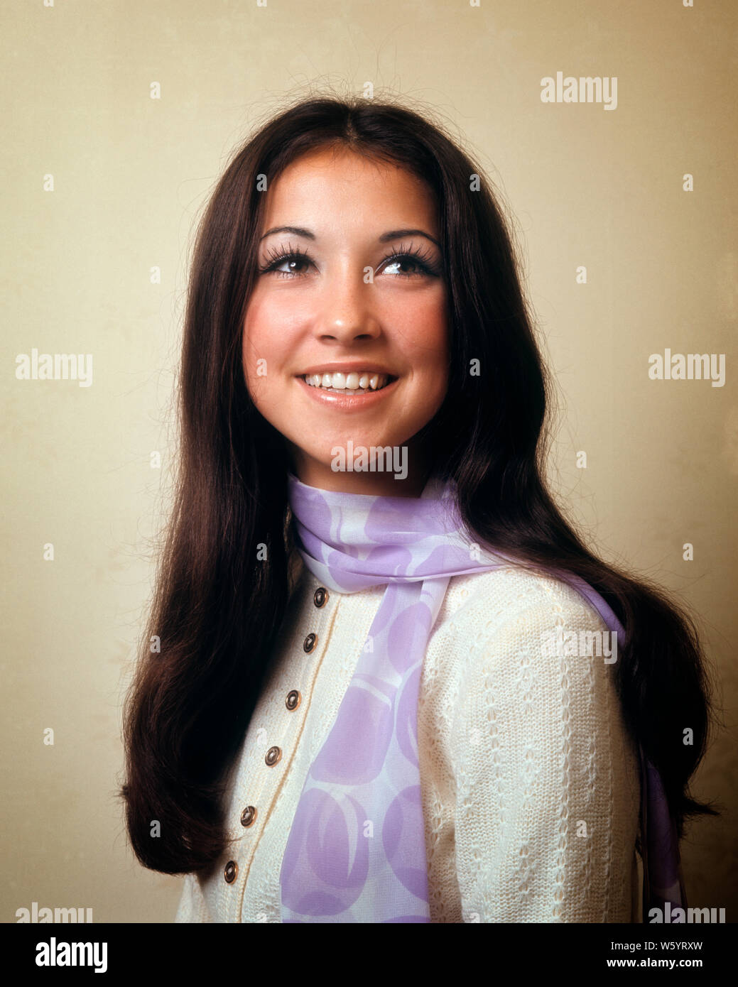 1970s PORTRAIT OF PRETTY SMILING TEEN GIRL WITH LONG BLACK HAIR WEARING WHITE SWEATER WITH LILAC SCARF GREAT EYE MAKEUP MASCARA - kg4650 HAR001 HARS STUDIO SHOT HEALTHINESS HOME LIFE COPY SPACE HALF-LENGTH MAKEUP PERSONS TEENAGE GIRL CONFIDENCE BRUNETTE PRETTY HAPPINESS CHEERFUL PRIDE SMILES JOYFUL LONG HAIR STYLISH TEENAGED BLACK HAIR BROWN EYES JUVENILES LILAC LOOKING UP MASCARA CAUCASIAN ETHNICITY HAR001 OLD FASHIONED Stock Photo