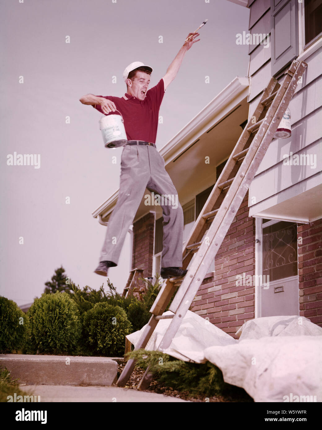 1960s HOUSE PAINTER MAN HOLDING PAINT CAN AND BRUSH ABOUT TO FALL OFF