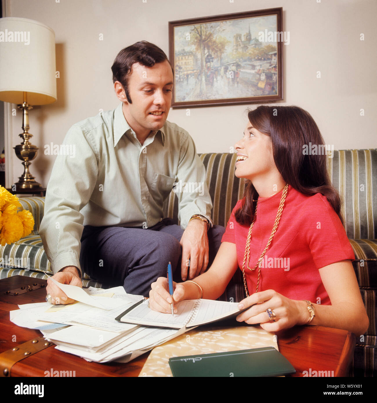 1970s SMILING COUPLE MAN WOMAN HUSBAND WIFE SITTING ON STRIPED COUCH REVIEWING FINANCES AND BILLS BALANCING CHECKBOOK CALENDAR  - ks7703 HAR001 HARS NOSTALGIA OLD FASHION FACIAL BUDGET COUCH STYLE COMMUNICATION TEAMWORK INFORMATION MYSTERY PLEASED JOY LIFESTYLE SATISFACTION FEMALES STRIPED MARRIED SPOUSE HUSBANDS HOME LIFE FINANCES COPY SPACE FRIENDSHIP HALF-LENGTH LADIES PERSONS MALES PLANNING CONFIDENCE PAYING EXPRESSIONS BALANCING PARTNER GOALS SUCCESS DREAMS HAPPINESS HEAD AND SHOULDERS CHEERFUL CHORE VICTORY STRATEGY AND LOW ANGLE PROGRESS CHECKBOOK ON FACIAL HAIR FEELING SMILES Stock Photo