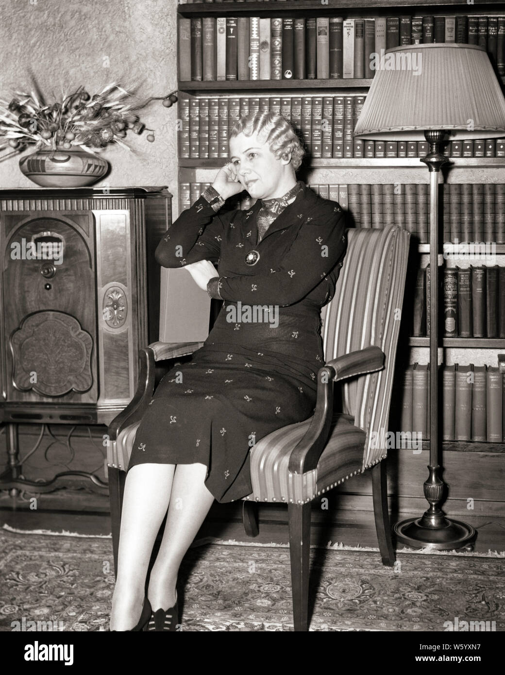 1930s MATURE WOMAN SITTING IN CHAIR LISTENING TO RADIO - r108 HAR001 HARS LEISURE AUDIO HAIRSTYLE MARCEL WAVE HOMES FINGER WAVES CONNECTION FLOOR LAMP RESIDENCE STYLISH BLACK AND WHITE CAUCASIAN ETHNICITY HAR001 OLD FASHIONED Stock Photo