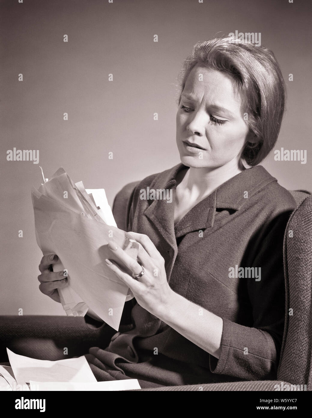 1960s WORRIED WOMAN HOLDING TWO HANDS FULL OF BILLS AND INVOICES SITTING READING AND LOOKING AT OVERWHELMING AMOUNT OF PAPERWORK - s15423 HAR001 HARS TROUBLE DEBT WORRY PROBLEM ABSTRACT LIFESTYLE FEMALES STUDIO SHOT MOODY HOME LIFE COPY SPACE HALF-LENGTH LADIES PERSONS RISK EXPRESSIONS TROUBLED B&W SADNESS EYE CONTACT HOMEMAKER HOMEMAKERS DISTRESSED AND AT OF CONCERN HOUSEWIVES MOOD GLUM AMOUNT ESCAPE BANKRUPT MISERABLE OVERWHELMING YOUNG ADULT WOMAN BLACK AND WHITE CAUCASIAN ETHNICITY HAR001 INVOICES OLD FASHIONED Stock Photo
