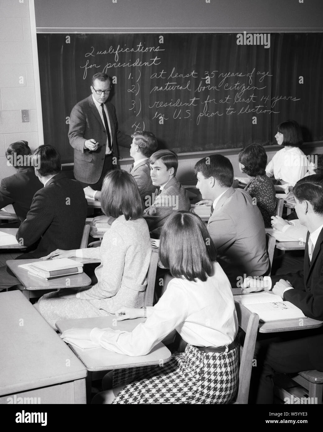 1960s MAN TEACHER IN HIGH SCHOOL CLASSROOM TEACHING A CIVICS OR HISTORY CLASS  WITH COED TEENAGE STUDENTS - s15388 HAR001 HARS NOSTALGIA OLD FASHION 1 JUVENILE TEACHERS COMMUNICATION INFORMATION LIFESTYLE HISTORY FEMALES JOBS COPY SPACE HALF-LENGTH PERSONS INSPIRATION MALES TEENAGE GIRL TEENAGE BOY CONFIDENCE B&W SKILL OCCUPATION SKILLS HIGH ANGLE INSTRUCTOR KNOWLEDGE OPPORTUNITY AUTHORITY HIGH SCHOOL OCCUPATIONS POLITICS HIGH SCHOOLS EDUCATOR TEENAGED OR EDUCATING EDUCATORS INSTRUCTORS JUVENILES MID-ADULT MID-ADULT MAN MID-ADULT WOMAN SCHOOL TEACHES TOGETHERNESS BLACK AND WHITE Stock Photo