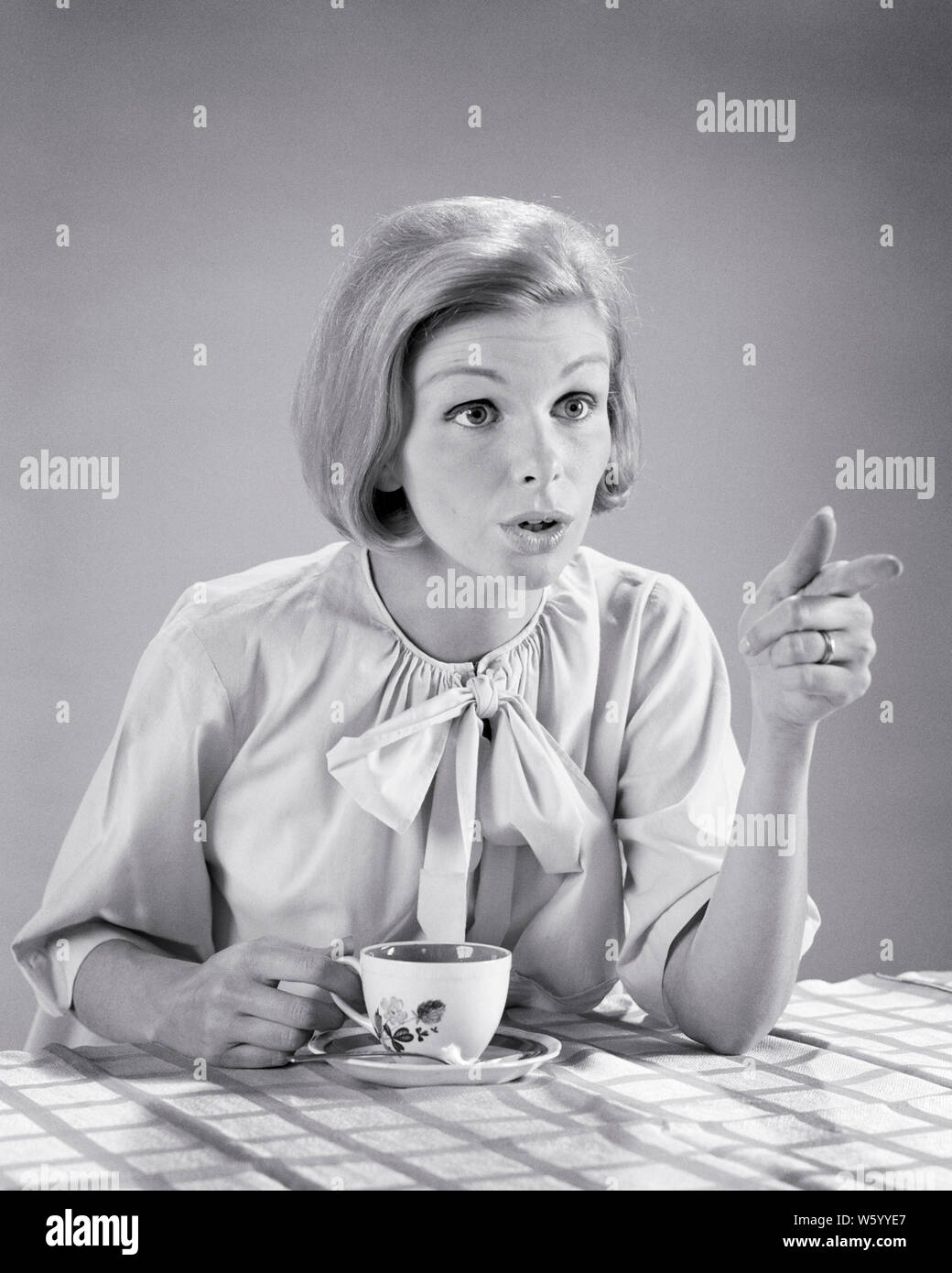 1960s BLONDE WOMAN DRINKING HER MORNING COFFEE TALKING ASSERTIVELY ACROSS BREAKFAST TABLE GESTURING POINTING HER FINGER - s15466 HAR001 HARS FACIAL ANGER COMMUNICATION BLOND YOUNG ADULT LIFESTYLE FEMALES STUDIO SHOT HOME LIFE COPY SPACE HALF-LENGTH LADIES PERSONS AFRAID FRIGHTENED CONFIDENCE GESTURING EXPRESSIONS TROUBLED AMAZED B&W MORNING HOMEMAKER BUG-EYED HOMEMAKERS DISAGREEMENT POWERFUL AUTHORITY DISAGREE GESTURES HOUSEWIVES CONCEPTUAL ACROSS FEARFUL SPAT EMPHATIC FEISTY WIDE-EYED BOLD INSISTENT QUARREL SQUABBLE STARTLED YOUNG ADULT WOMAN ALARMED BLACK AND WHITE CAUCASIAN ETHNICITY HAR001 Stock Photo