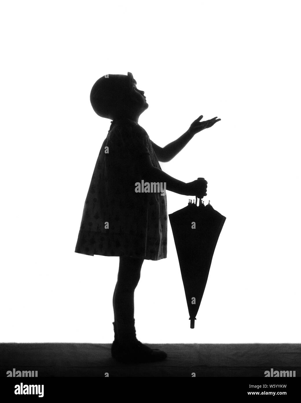 1920s ANONYMOUS SILHOUETTE OF LITTLE GIRL WEARING CLOCHE HAT HOLDING AN UMBRELLA PUTTING OUT HAND TO SEE IF SHE FEELS RAINDROPS - s1695 HAR001 HARS STUDIO SHOT SEE HOME LIFE COPY SPACE FULL-LENGTH RAINY CARING RAINING SYMBOLS SILHOUETTES CONFIDENCE B&W OUTLINE DISCOVERY SILHOUETTED CLOCHE SHE TO ANTICIPATION CONCEPT CONCEPTUAL STYLISH ANONYMOUS SYMBOLIC CONCEPTS COOPERATION IF JUVENILES KONE RAINDROPS BLACK AND WHITE HAR001 OLD FASHIONED PRECIPITATION REPRESENTATION Stock Photo