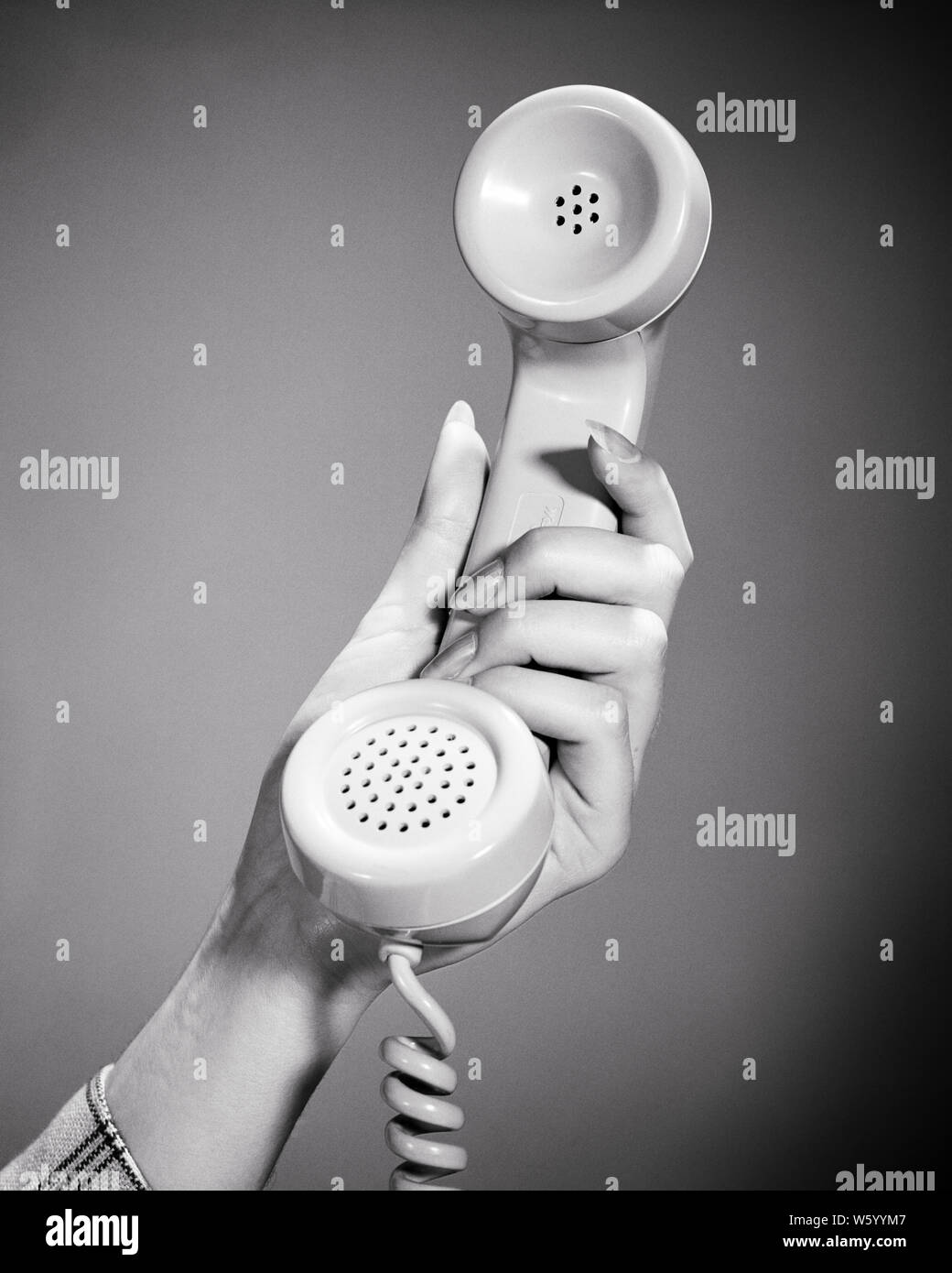 1950s 1960s 1970s WOMAN HAND HOLDING CLASSIC TELEPHONE COMMUNICATIONS HANDSET FOR LISTENING AND SPEAKING  - s16948 HAR001 HARS STUDIO SHOT RURAL HOME LIFE COPY SPACE LADIES PERSONS SYMBOLS B&W LEISURE PROTECTION STRATEGY CUSTOMER SERVICE AND NETWORKING LOW ANGLE POWERFUL OPPORTUNITY CONCEPT CONNECTION CONCEPTUAL STYLISH SUPPORT HANDSET SYMBOLIC COMMUNICATIONS CONCEPTS RELAXATION YOUNG ADULT WOMAN BLACK AND WHITE CAUCASIAN ETHNICITY HANDS ONLY HAR001 OLD FASHIONED REPRESENTATION Stock Photo