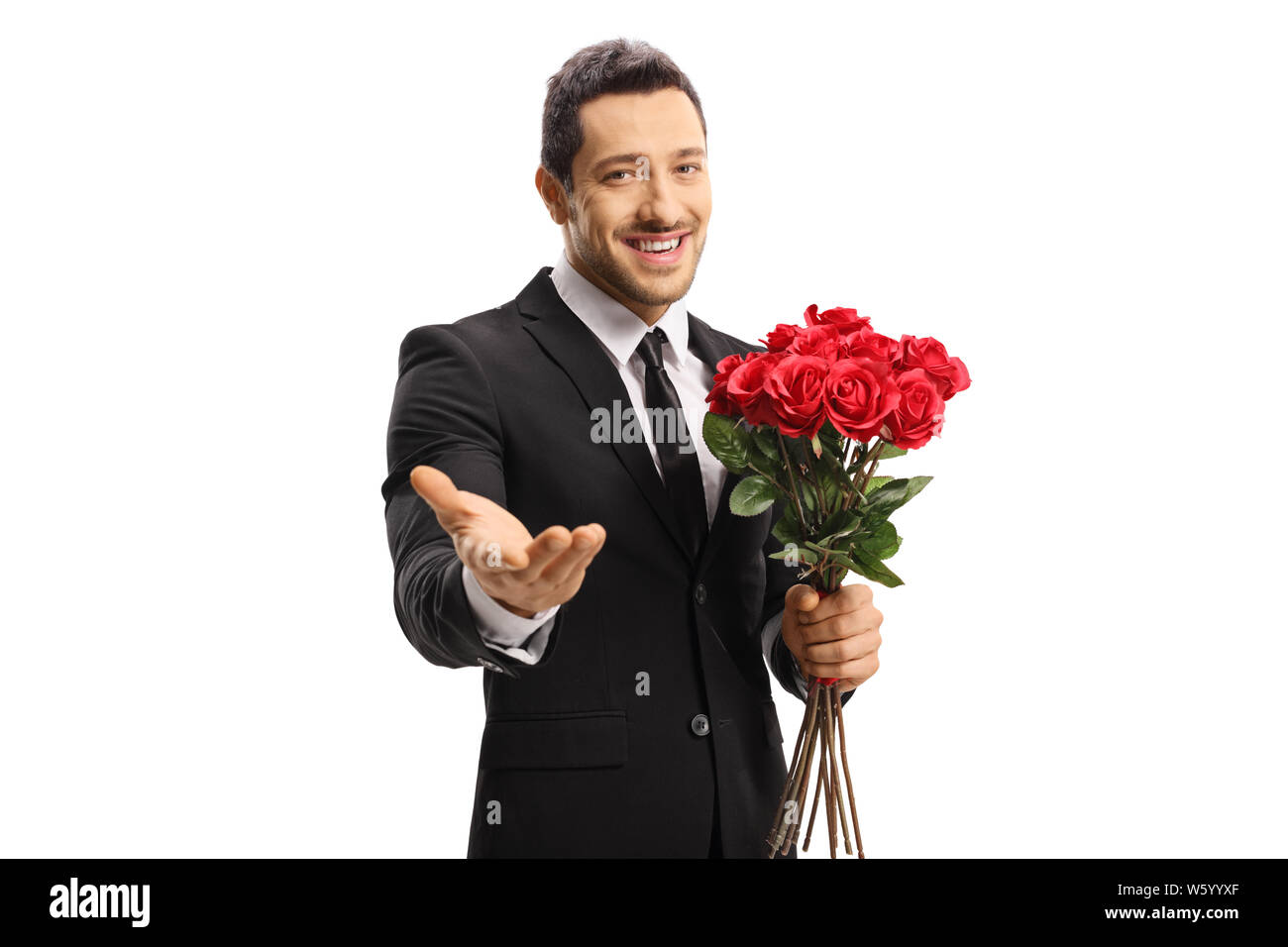 Handsome young man in a suit holding a bunch of red roses and showing