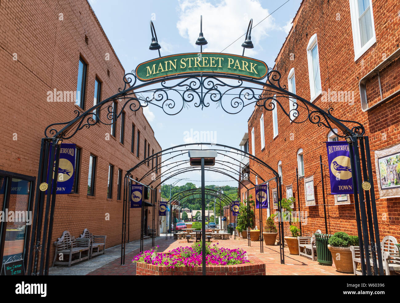 RUTHERFORD, NC, USA-27 JULY 19: A colorful urban park with flowers and greenery is bounded by two brick buildings. Stock Photo