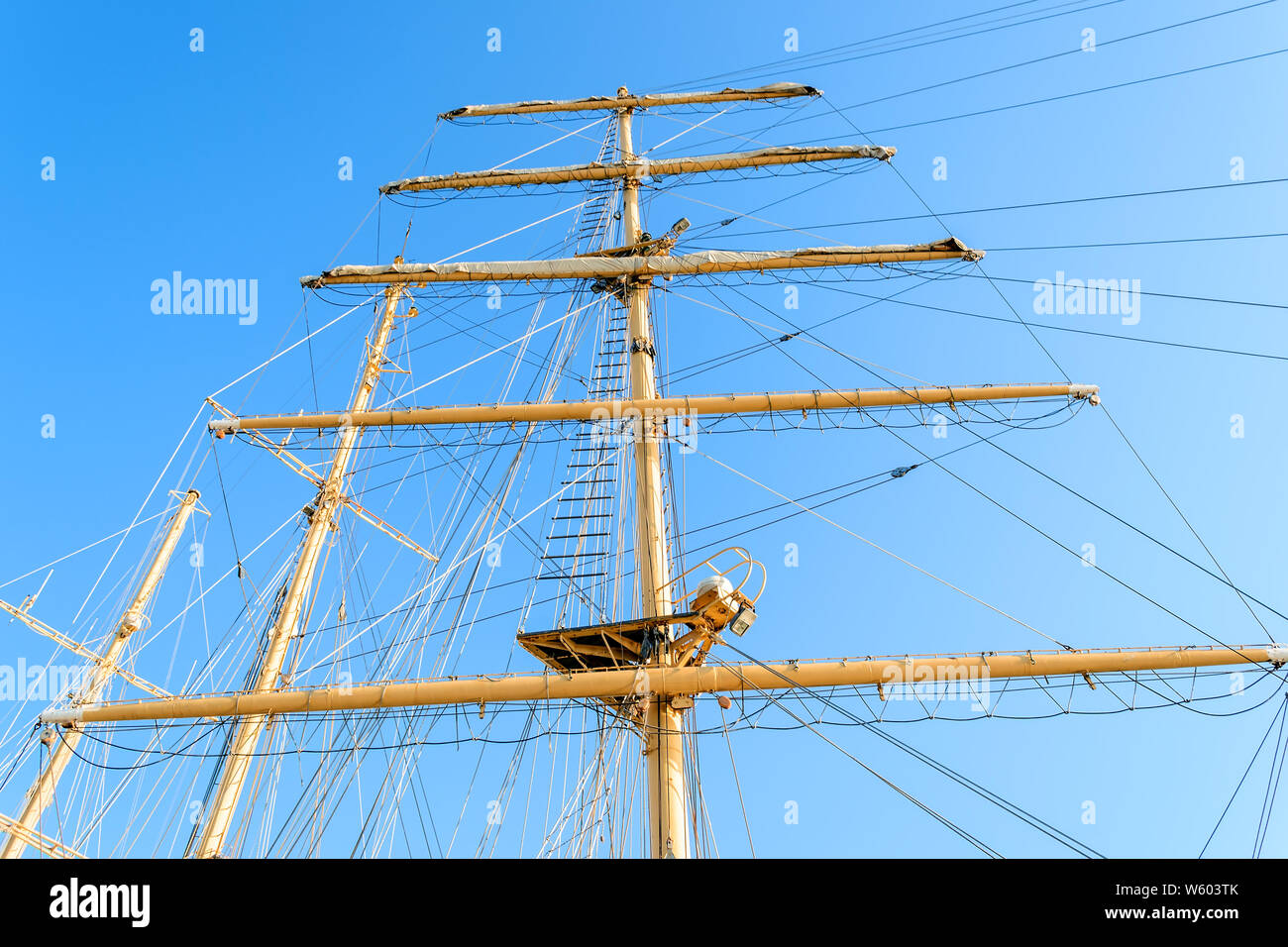 Bottom view of the mast, sail yards with the lowered sails and rigging of a sailing ship against a clear sky on a sunny day. Stock Photo