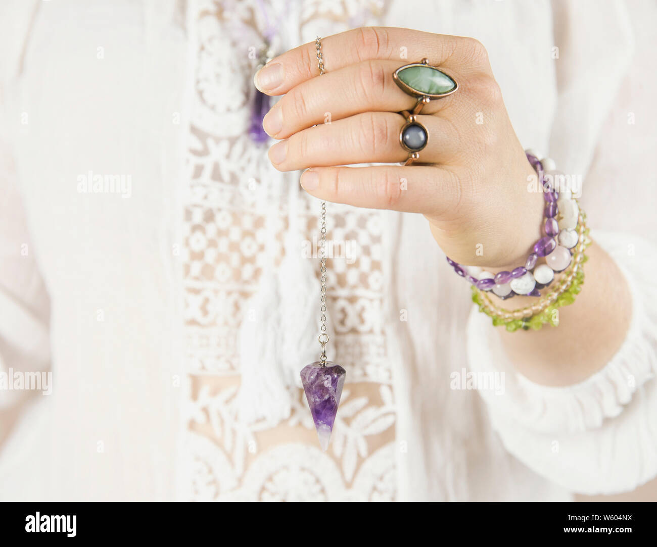 Spiritual healer using purple natural Amethyst crystal quartz pendulum. Close up view, white background. Stock Photo