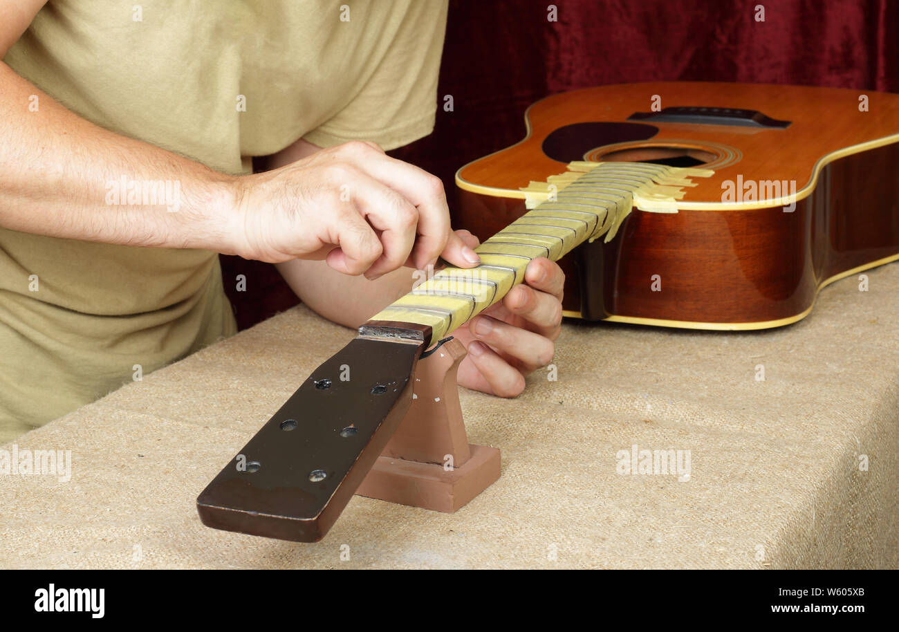 Musical instrument guitar repair and service - Worker polishing guitar neck frets acoustic guitar sandpaper Stock Photo