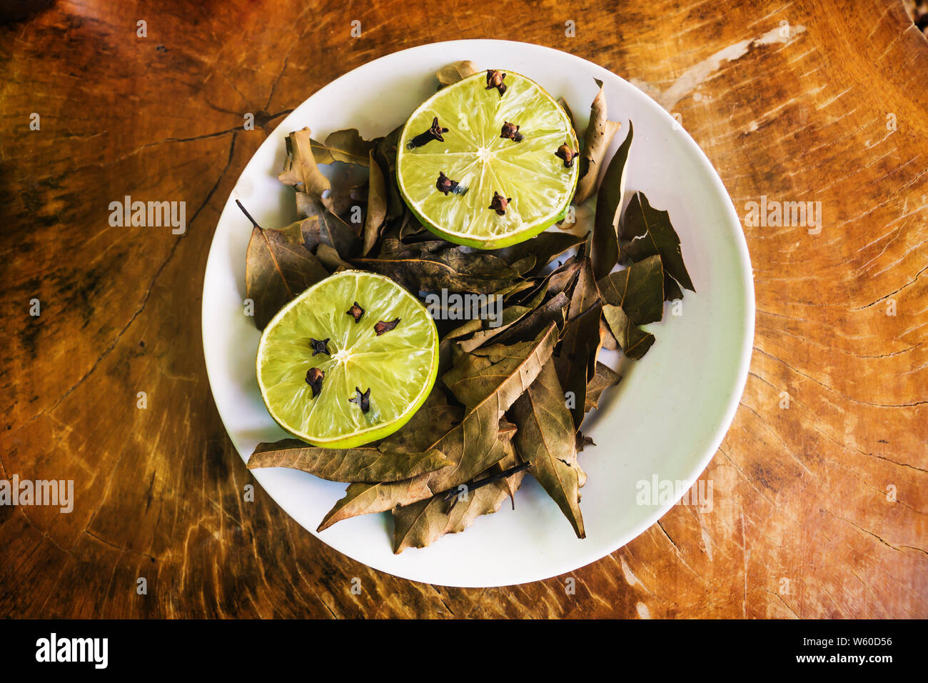 Natural repellent white plate with fresh lime, cloves and dried laurel on wooden table Stock Photo