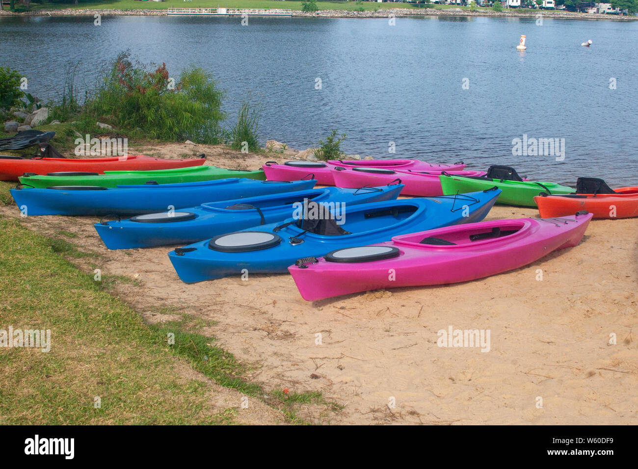Colorful Kayaks on sandy beach next to lake, ready for outdoor activities Stock Photo
