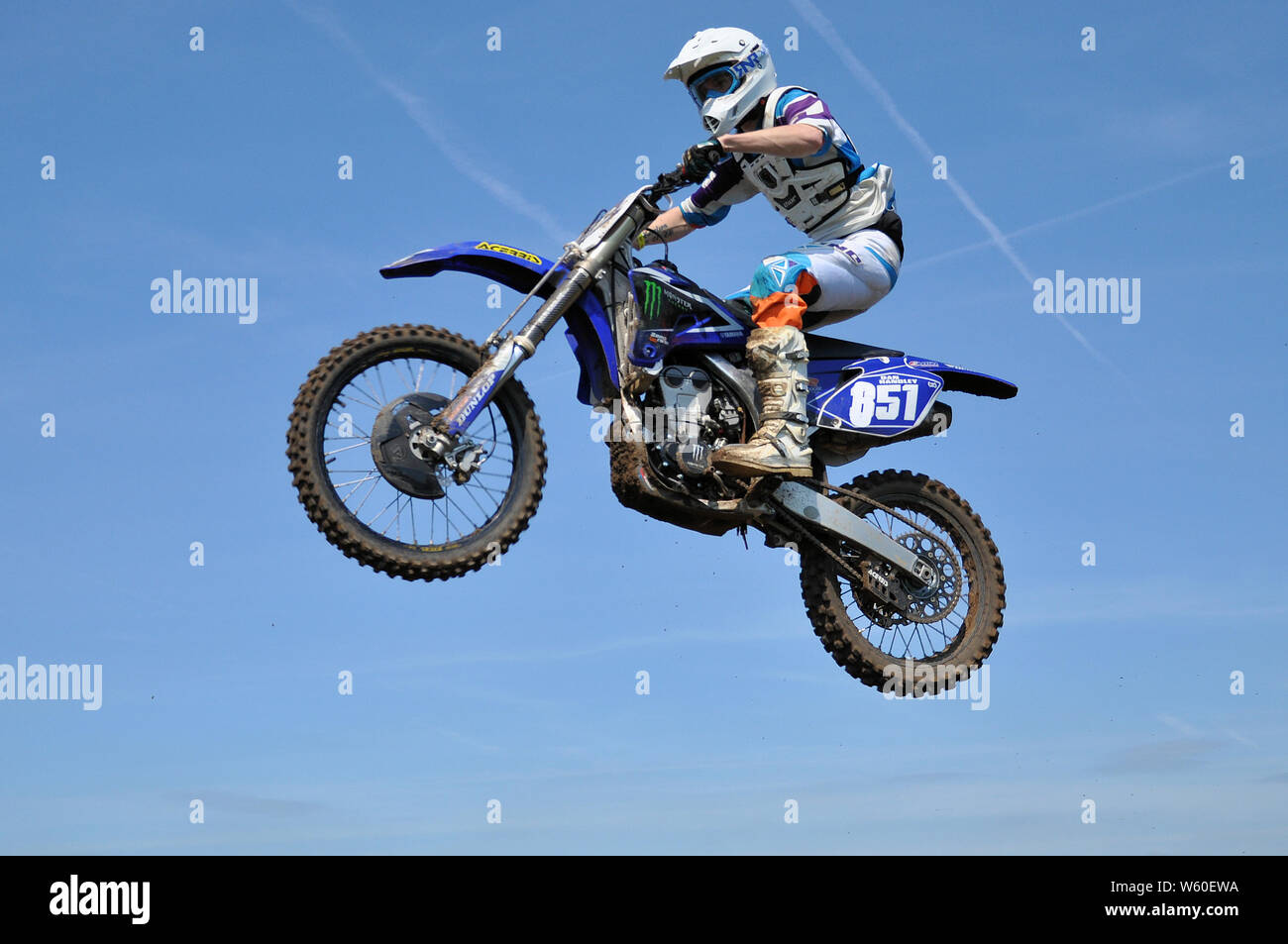 Motorbike rider on scramble bike, jumping high in blue sky. Motocross is a form of motorcycle racing held on rough off-road circuits. Dirt bike mx Stock Photo