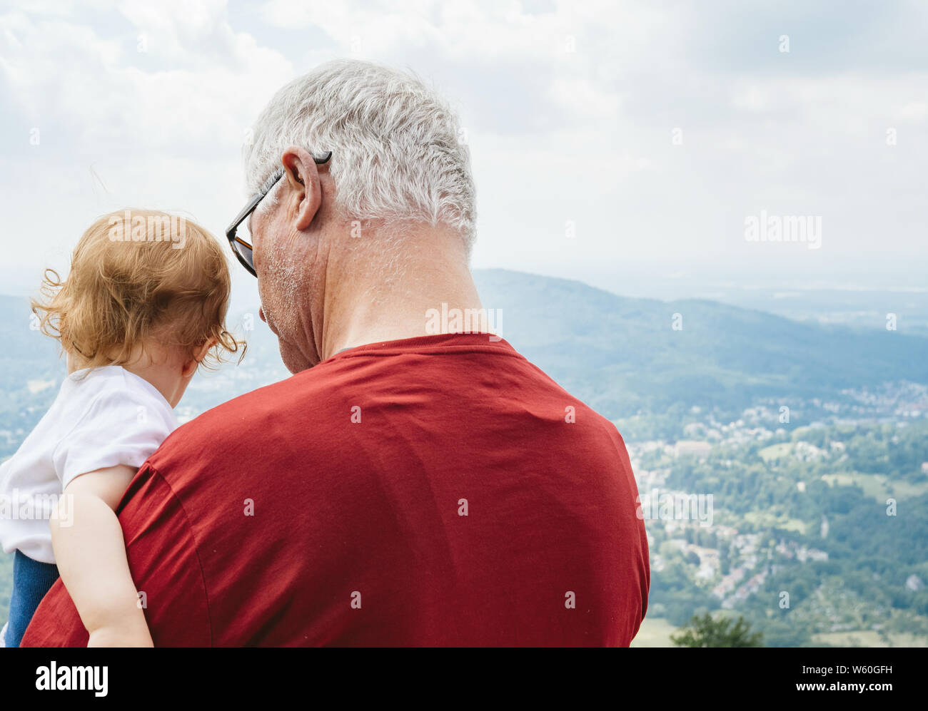 Baden-Baden, Germany - Jul 7, 2019: Rear view of senior male grandfather with white hair holding little child Stock Photo