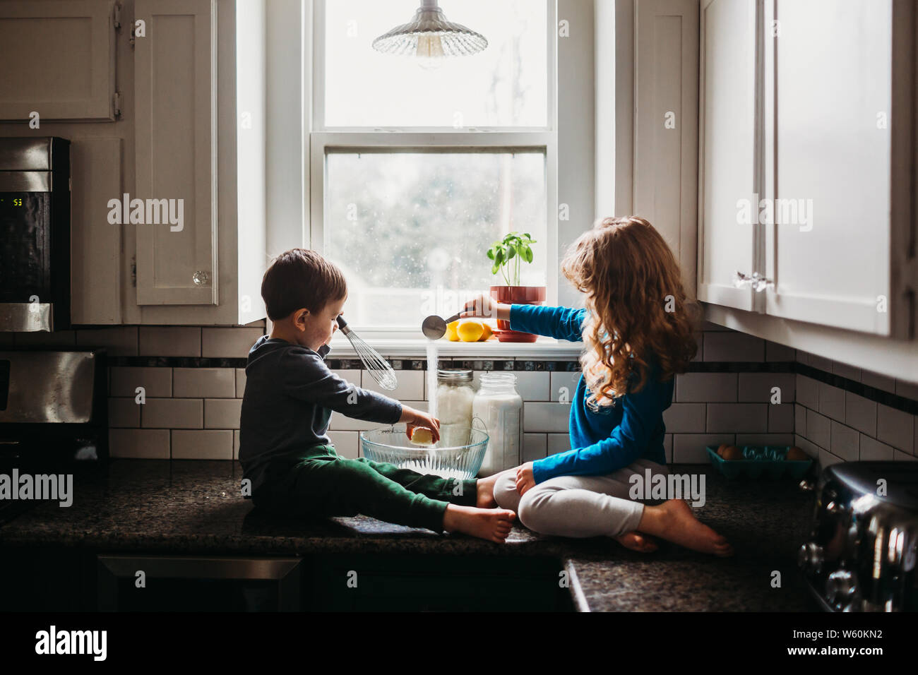 Baby boy playing on kitchen counter with strainer over his head Stock Photo