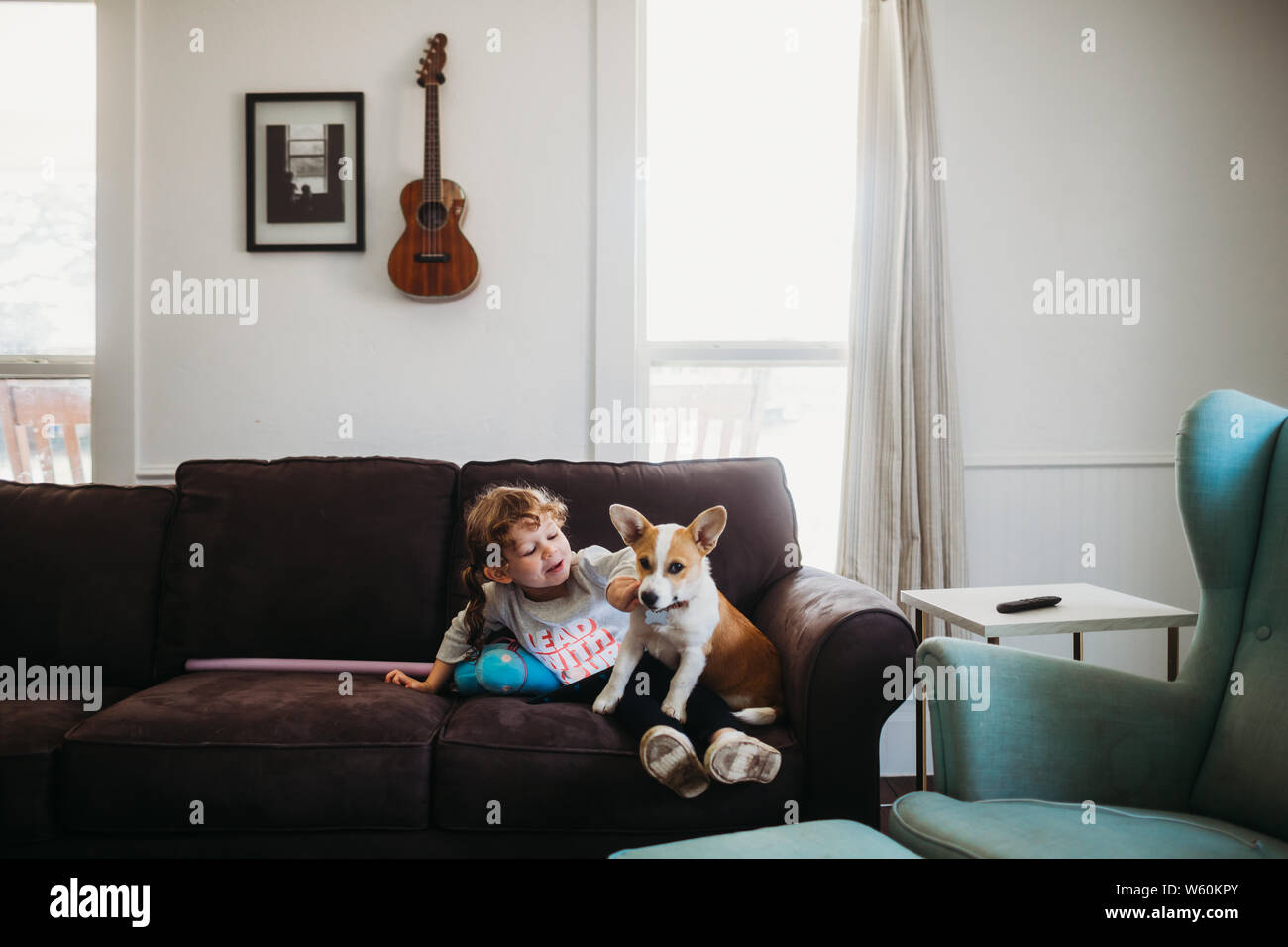 Young girl playing with corgi puppy on couch in living room Stock Photo