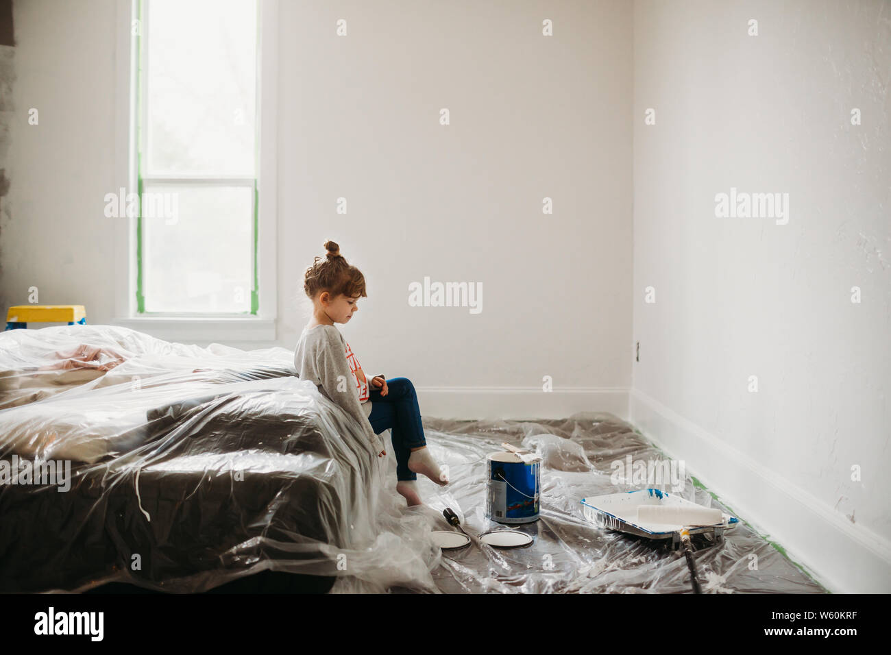 Young girl sitting on bed in freshly painted white room Stock Photo
