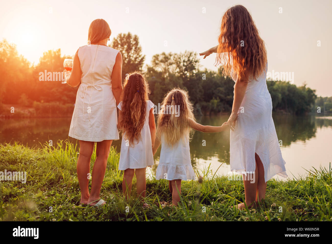 Family walking by summer river at sunset. Mother, grandmother and kids admiring landscape after picnic. Three denerations Stock Photo