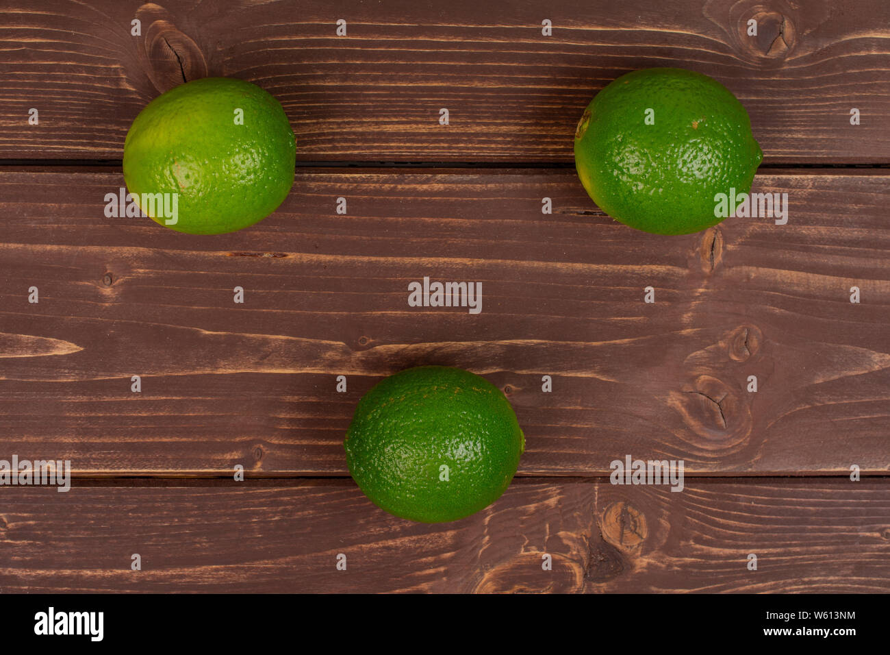 Group of three whole fresh green lime flatlay on brown wood Stock Photo