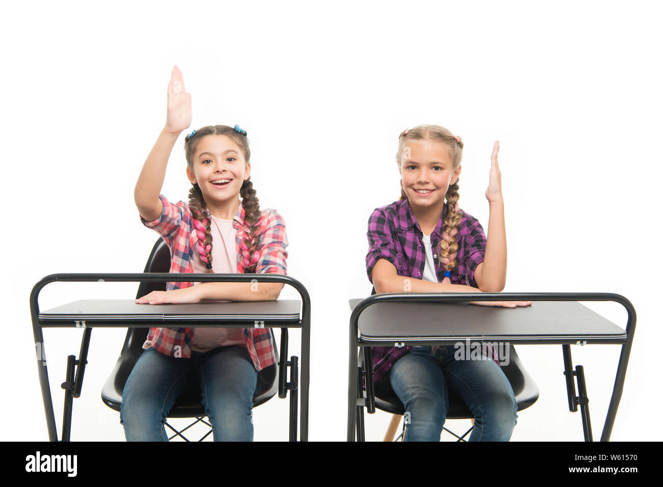 Free or private schooling. Little children enjoy home schooling. Small schoolgirls having compulsory schooling. Adorable kids with raised hands sitting at desks isolated on white. Schooling years. Stock Photo