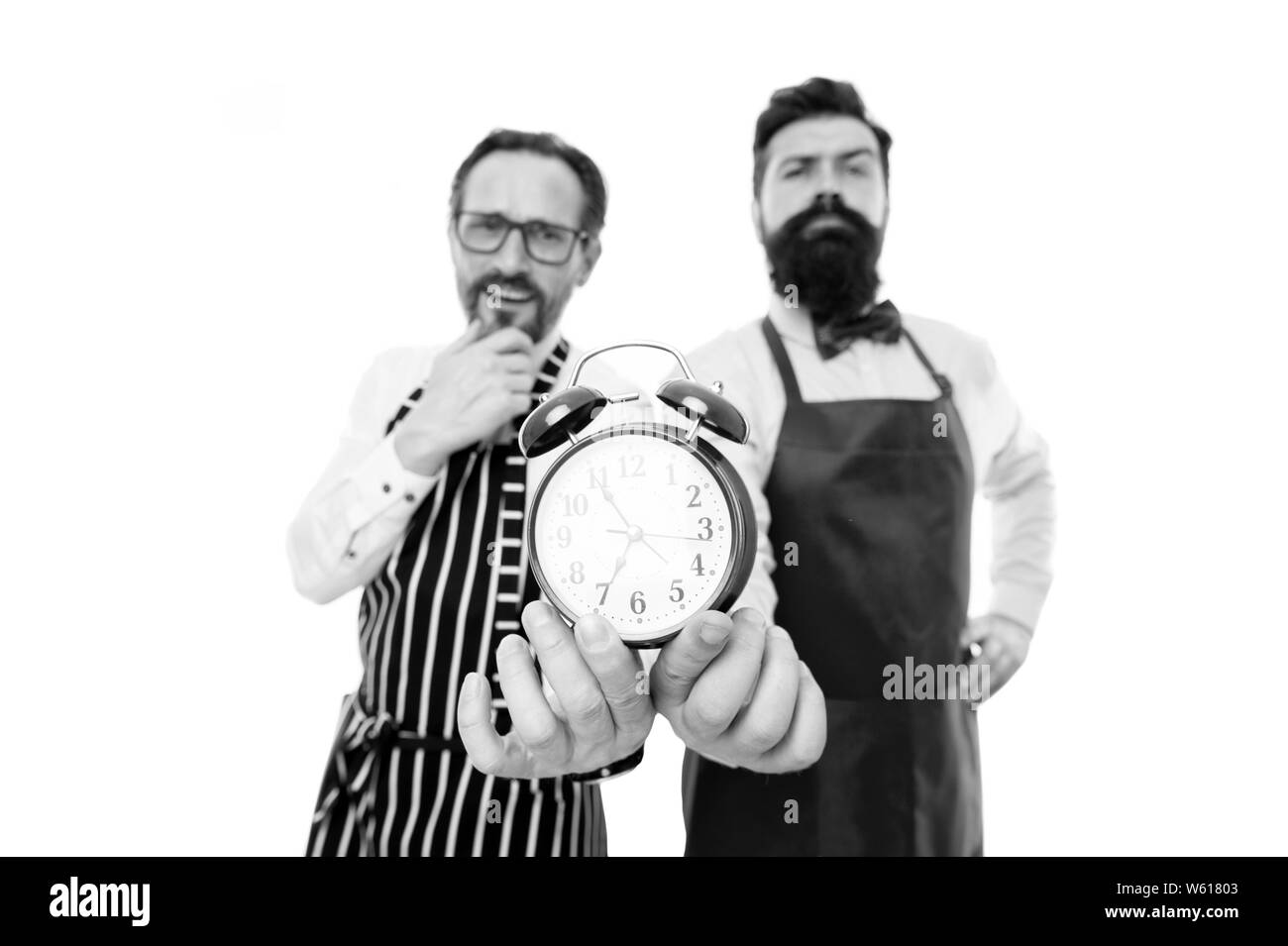 Man bearded hipster and mature chef apron white background. Working hours and lunch break. Lack of time. Check what time is it. It is lunch time. Men cooks with alarm clock. Perfect discipline. Stock Photo