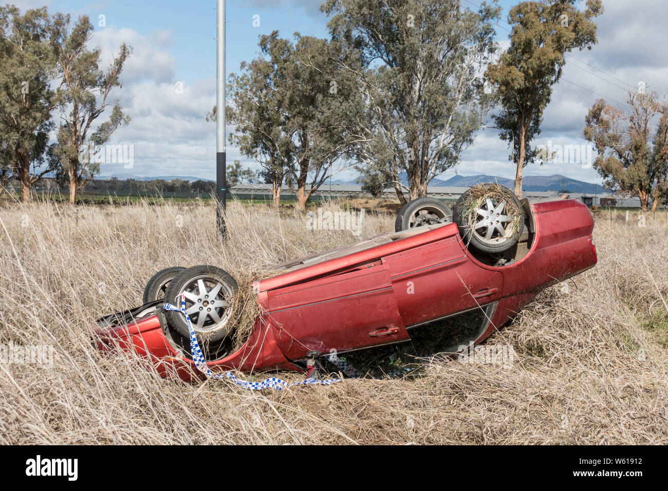 Red Mitsbishi Magna car in roll over crash on country road, Australia. Stock Photo