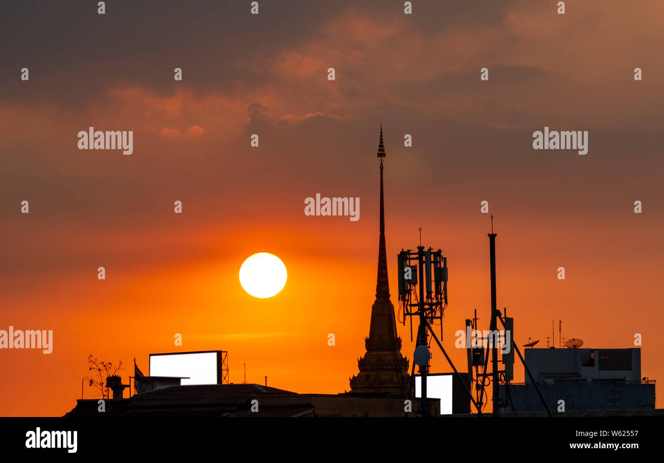 Beautiful sunset sky over the city. Silhouette temple building and telecommunication tower. Antenna on sunset sky background. Radio and satellite pole Stock Photo
