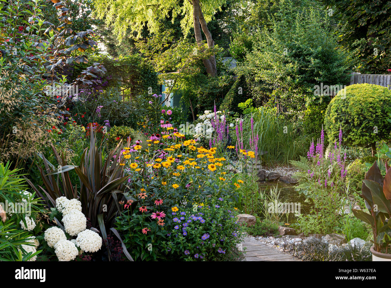Mixed flower border with garden pond, in an English suburban garden. Stock Photo
